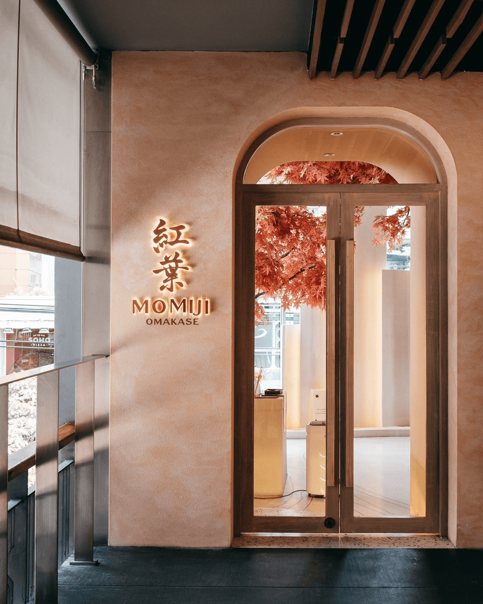 The arched entrance to Momiji Omakase, with the 紅葉 sign lit against a plaster wall